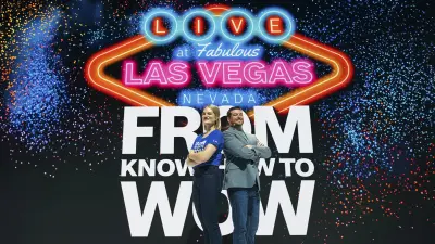 The two podcast hosts Melena and Geoff stand on stage in front of a large Las Vegas-style From KNOW-HOW to WOW logo.