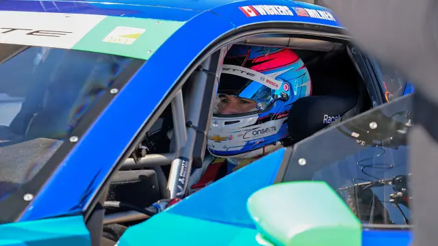 Robert Wickens in his racing outfit and helmet behind the wheel of his car.