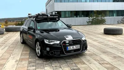 A black test vehicle parks in front of a building.