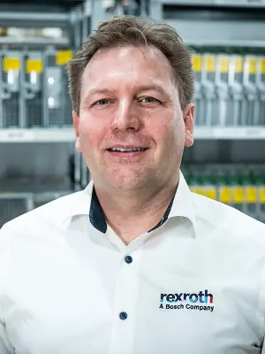 Porträt von Daniel Voegeli von Bosch Rexroth vor Regalen mit Elektronikkomponenten.