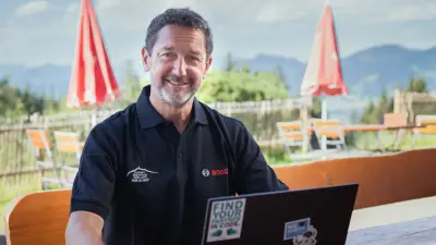 Reiner sitzt an seinem Schreibtisch vor seiner Berghütte und arbeitet.