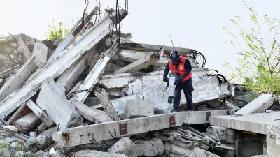 Eine Person in roter Warnweste arbeitet mit einem Presslufthammer in den Trümmern eines Gebäudes.