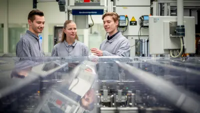 Group of people in work coats talking next to production equipment.