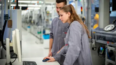 Two people at a computer station in a production line reviewing information.