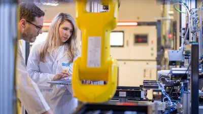 Two people in lab coats working together near yellow robotic equipment.