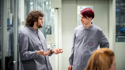 Two people in work coats talking inside a production area.