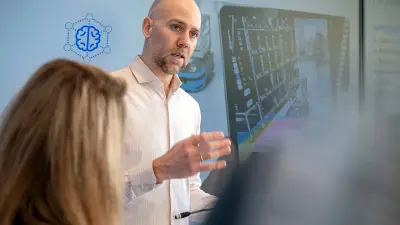 Person presenting in front of a screen with industrial graphics.