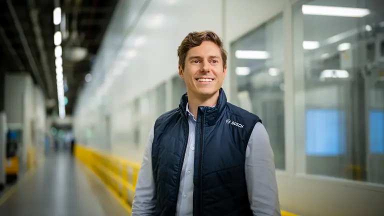 Person standing in a production hallway wearing a branded vest.
