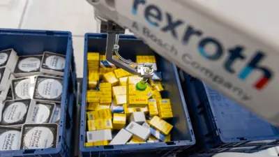 Auf dem Bild ist ein Roboterarm von Bosch Rexroth zu sehen, der ein kleines Päckchen aus einer Kiste greift.