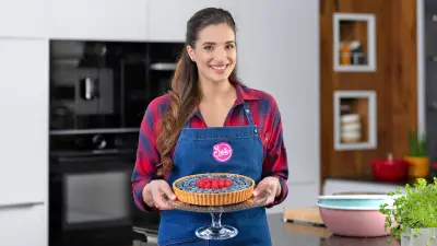 Die Food-YouTuberin Sally Özcan präsentiert in ihrer Küche lächelnd eine fertig gebackene und mit Beeren verzierte Zitronentarte.