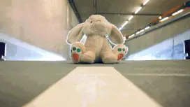 A toy bunny sits in the middle of a parking garage aisle. Headlights in the background indicate that a car is approaching.