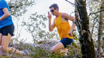 Extreme athlete Till Schenk runs past a tree while tapping his smartglasses with his right hand. A second female athlete can be seen on the left of the picture.