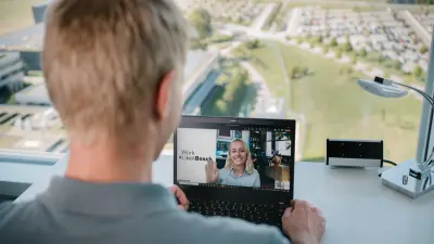 Das Testimonial Joachim ist von hinten zu sehen. Er sitzt vor einem Fenster an einem Tisch, auf dem sich eine Schreibtischlampe und ein Laptop befinden. Auf dem Laptop-Bildschirm ist eine Frau zu sehen, mit der er über den Laptop spricht.