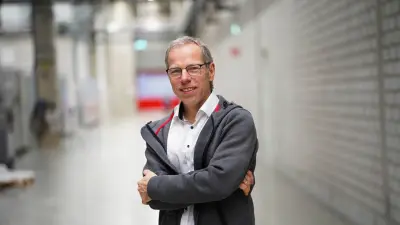 Dr. Thomas Waldenmaier is a senior expert in technology development and heat treatment processes at Bosch Research. He is responsible for the process development and modelling of thermo-chemical heat treatment processes. He stands in a hallway of a plant, facing the camera while smiling with crossed arms. He is wearing a white shirt and the Bosch Research jacket. 