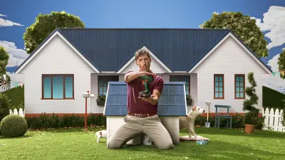 Shawn poseert in de voortuin voor een hondenhok met zijn boorgereedschap in de hand.