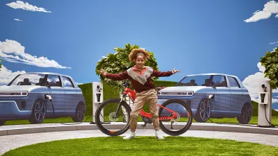 Shawna poseert voor haar eBike, terwijl de elektrisch aangedreven auto's bij oplaadpunten op de achtergrond te zien zijn.