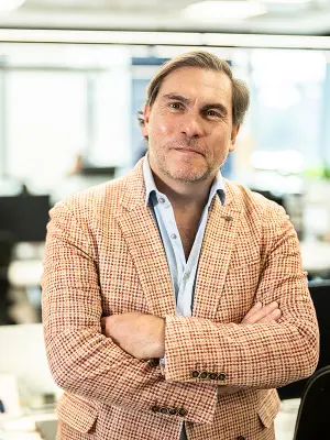 CEO of BSH Egypt Luis Alvarez can be seen in the foreground with his arms crossed. He is wearing a white and red checked jacket with a light blue shirt underneath and grins into the camera. In the background, the office space of BSH Egypt can be seen.