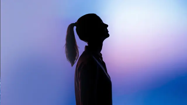 The silhouette of a woman with a ponytail against a blurred background. 