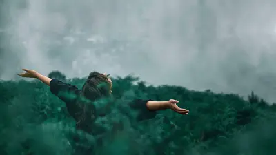 A person standing in front of a wall of fog amongst head-high plants with their arms extended. 