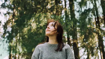A woman standing in a forest, looking up.
