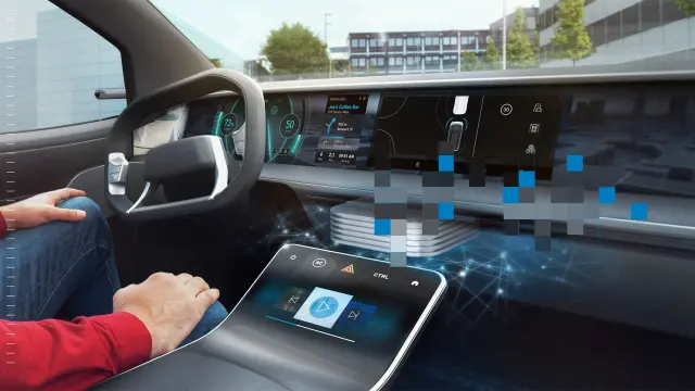 A person sits in a car using a touchscreen display. Parts of the dashboard are overlaid with colorful pixel blocks.