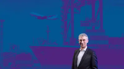 Frank Appel vor einem blauen Hintergrund auf dem Motive zur Mobilität zu sehen sind.