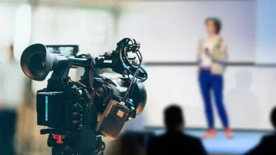 A woman on stage (blurred) is filmed by a camera in the foreground (sharp).