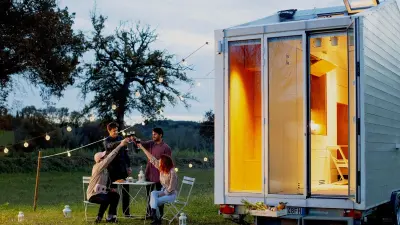 Architect Leonardo Di Chiara stands in front of the tiny house at dusk, toasting a successful day with friends.