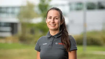 Bosch simulation and calculation engineer Tsvetelina Yordanova in a Bosch polo shirt can be seen in the foreground. The Bosch Research Renningen site is visible, blurred, in the background.