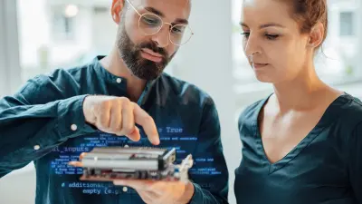 Two Bosch researchers examine a technological device with interest. A Keras code can be seen around the device, illustrating the artificial intelligence inside.