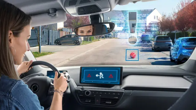 One woman sits in a car. An AI program throws her a visual cue on the windshield that there is a ball on the road. A Keras code traces the outline of a child, indicating that there may be danger.