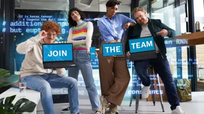 Four young people stand next to each other, motivated. Each is holding a digital device such as a laptop or smartphone. The displays show different words that together form the sentence "Join the Team". ("Join the team")