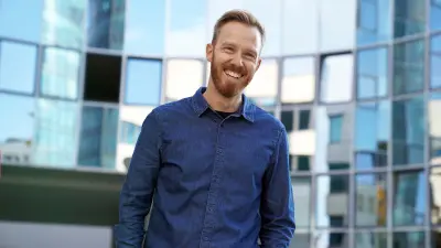 Christoph Dörr stands in front of many windows, wears a blue denim shirt and smiles into the camera.