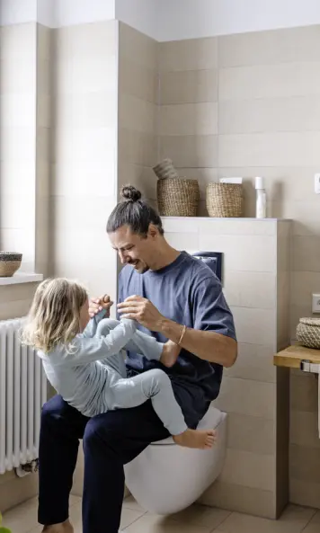 Ein Vater spielt mit seinem Kind in einem modernen Badezimmer, während die Mutter zusieht.