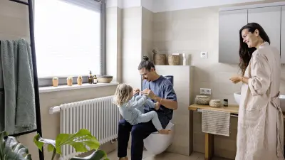 A father plays with his child in a modern bathroom while the mother looks on.