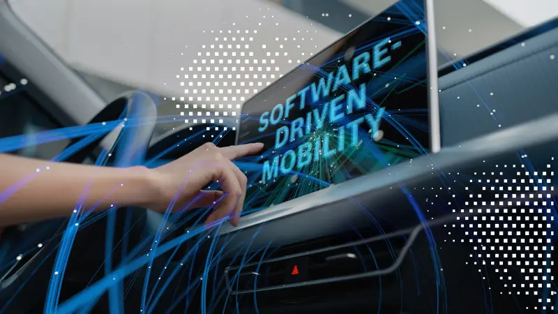A hand taps on a vehicle display showing the large text “SOFTWARE-DRIVEN MOBILITY”; dynamic square codes overlay the image.