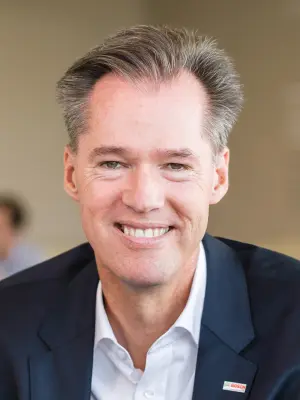 Ein professionelles Porträt eines lächelnden Markus Heyn im Anzug, frontal aufgenommen vor neutralem Hintergrund.