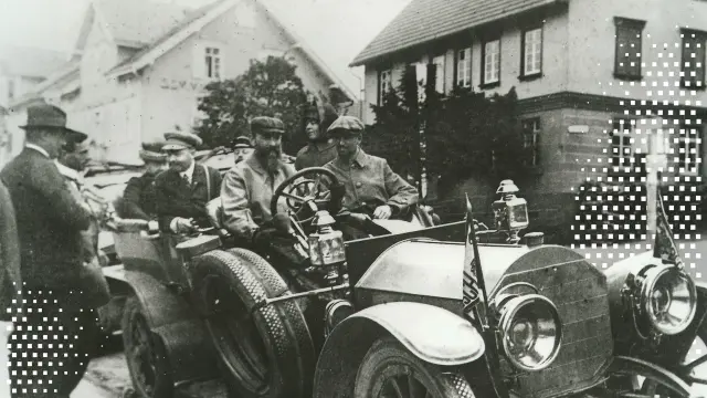 Ein historisches Schwarz-Weiß-Foto mit Menschen in einem frühen Automobil, überlagert von modernen quadratischen Pixel-Codes.