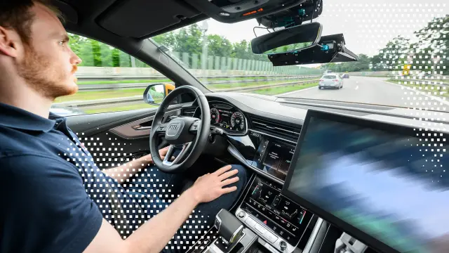 Ein Fahrer sitzt am Steuer eines Autos auf der Autobahn; eine transparente digitale Überlagerung mit quadratischen Pixelcodes liegt über dem Displaybereich.