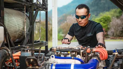 Sportlicher Mann im schwarzen T-Shirt mit Sonnenbrille und Handschuhen blickt auf eingebauten Motor unter der gekippten Kabine eines Lkw