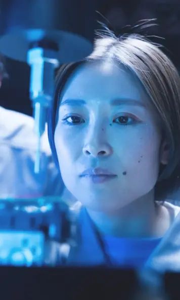 Eine Person im Laborkittel mit Pipette unter blauem Licht; Gesicht teilweise von grafischen Flächen verdeckt.