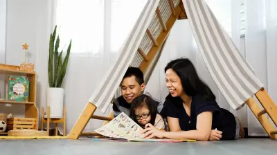 Der Handwerker Brian Tan, seine Frau und seine Tochter liegen unter einer Holzkonstruktion. Sie lachen und lesen ein Kinderbuch.