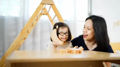 Ein Mädchen mit Down-Syndrom und seine Mutter spielen mit Holzklötzen.