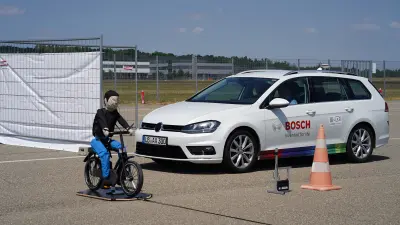 Test vehicle with Bosch branding stops near a bicycle dummy during an automated driving safety test.