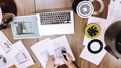 Ein Schreibtisch mit Laptop und verschiedenen Designskizzen von Vitesy.
