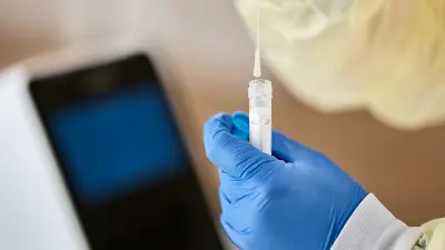 A swab is inserted into a reagent container by a hand in a rubber glove.