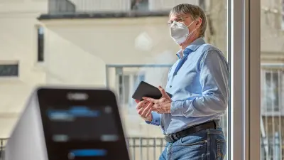 Clemens Weller is standing at the window with a tablet in his hand, in front of him we see the PCR diagnostic platform Vivalytic.