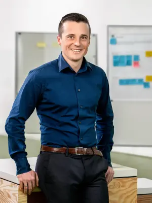 Person in blue shirt leaning on desk in office, whiteboards with notes behind