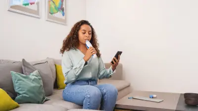 Person on sofa using breath device, smartphone in hand, table in front