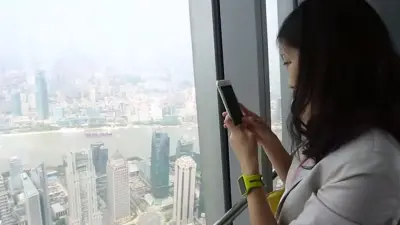The image shows a woman with smartwatch inside a tower overlooking the skyline of shanghai.